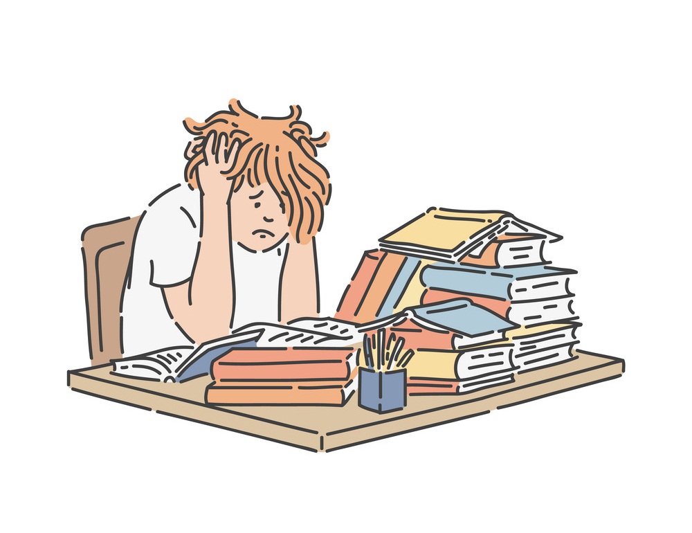Stressed school student sitting at table with pile of books and studying.